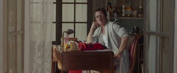 Movie still from “By the Sea” (2015), directed by Angelina Jolie – A man sitting at a desk in front of an open window; Medium shot, Low angle
