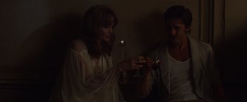 Movie still from “By the Sea” (2015), directed by Angelina Jolie – A woman holding a wine glass while standing next to a man; Medium shot, Low angle