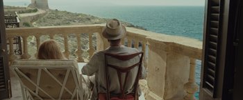 Movie still from “By the Sea” (2015), directed by Angelina Jolie – A man sitting on top of a chair looking out at the ocean; Medium shot, High angle