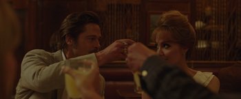 Movie still from “By the Sea” (2015), directed by Angelina Jolie – A group of people sitting at a table with drinks; Medium shot, Over the shoulder angle