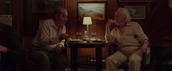 Movie still from “By the Sea” (2015), directed by Angelina Jolie – Two men sitting at a table with wine glasses and a lamp; Medium shot, High angle
