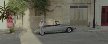 Movie still from “By the Sea” (2015), directed by Angelina Jolie – An older man sitting on the hood of a convertible car; Wide shot, High angle