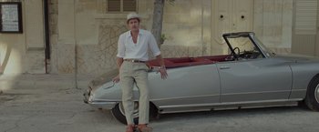 Movie still from “By the Sea” (2015), directed by Angelina Jolie – A man standing next to an old fashioned car; Wide shot, High angle