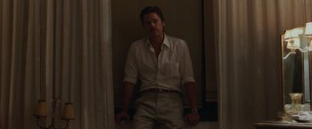 Movie still from “By the Sea” (2015), directed by Angelina Jolie – A man in a white shirt standing in a room; Medium shot, Low angle