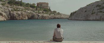 Movie still from “By the Sea” (2015), directed by Angelina Jolie – A man sitting on the beach looking at a house; Wide shot, Over the shoulder angle