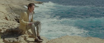 Movie still from “By the Sea” (2015), directed by Angelina Jolie – A man sitting on a rock near the ocean; Wide shot, High angle