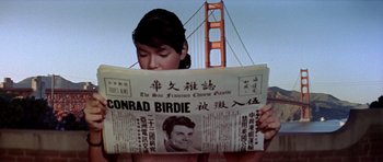 Movie still from “Bye Bye Birdie” (1963), directed by George Sidney – A woman reading a newspaper in front of the golden gate bridge in san francisco; Close Up shot, High angle