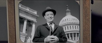 Movie still from “Bye Bye Birdie” (1963), directed by George Sidney – A man in a suit and tie standing in front of a building; Medium shot, Low angle
