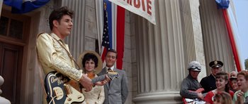 Movie still from “Bye Bye Birdie” (1963), directed by George Sidney – A man and a woman holding a guitar in front of an american flag; Medium shot, Low angle
