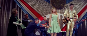 Movie still from “Bye Bye Birdie” (1963), directed by George Sidney – A woman in a green polka dot dress standing next to a man in a black suit; Medium shot, Low angle