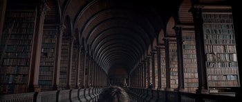 Movie still from “Byzantium” (2012), directed by Neil Jordan – A person is sitting in a library with a lot of bookshelves; Medium shot, Low angle