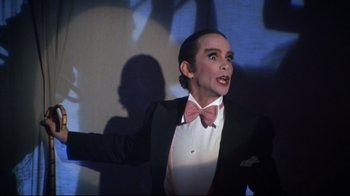 Movie still from “Cabaret” (1972), directed by Bob Fosse – A man in a suit and bow tie standing in front of a wall; Close Up shot, Low angle