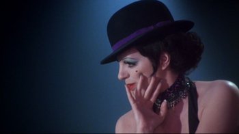 Movie still from “Cabaret” (1972), directed by Bob Fosse – A woman in a purple hat and a purple necklace; Close Up shot, Over the shoulder angle