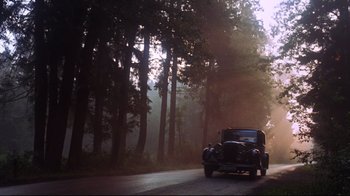 Movie still from “Cabaret” (1972), directed by Bob Fosse – An old car driving down a road in the woods; Extreme Wide shot, Low angle