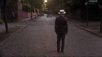 Movie still from “Cabaret” (1972), directed by Bob Fosse – A man in a suit and hat is standing in the middle of the street; Wide shot, High angle