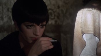 Movie still from “Cabaret” (1972), directed by Bob Fosse – A woman smoking a cigarette while looking at the camera; Close Up shot, Over the shoulder angle