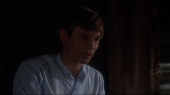 A man in a white shirt is sitting in a dark room
