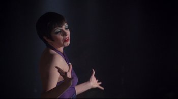 Movie still from “Cabaret” (1972), directed by Bob Fosse – A woman in a purple dress standing in a dark room; Close Up shot, Over the shoulder angle