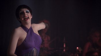 Movie still from “Cabaret” (1972), directed by Bob Fosse – A woman in a purple dress is singing; Medium shot, Over the shoulder angle