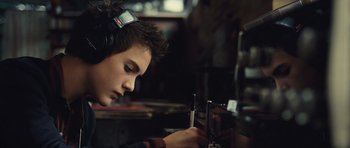 Movie still from “Café de Flore” (2011), directed by Jean-Marc Vallée – A young man wearing headphones looking at an electronic device; Close Up shot, High angle