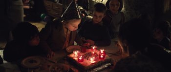 Movie still from “Café de Flore” (2011), directed by Jean-Marc Vallée – A group of people sitting around a cake with lit candles on it; Medium shot, High angle