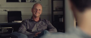 Movie still from “Café de Flore” (2011), directed by Jean-Marc Vallée – A man sitting in a chair smiling for the camera; Close Up shot, Over the shoulder angle