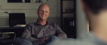 Movie still from “Café de Flore” (2011), directed by Jean-Marc Vallée – A man sitting in a chair smiling for the camera; Close Up shot, Over the shoulder angle