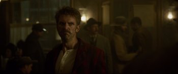 Movie still from “The Call of the Wild” (2020), directed by Chris Sanders – A man in a red jacket standing in a room with other men; Close Up shot, Over the shoulder angle