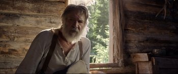 Movie still from “The Call of the Wild” (2020), directed by Chris Sanders – An old man with a beard is holding a guitar in front of a window; Medium shot, Over the shoulder angle