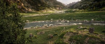 Movie still from “The Call of the Wild” (2020), directed by Chris Sanders – A grassy area with a river running through it and mountains in the background; Extreme Wide shot, High angle