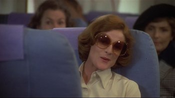 Movie still from “California Suite” (1978), directed by Herbert Ross – A woman sitting on a seat on an airplane wearing sunglasses; Close Up shot, Over the shoulder angle