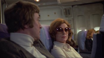 Movie still from “California Suite” (1978), directed by Herbert Ross – A man and a woman sitting on a seat on an airplane; Medium shot, Over the shoulder angle