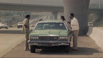 Movie still from “California Suite” (1978), directed by Herbert Ross – A couple of people that are standing next to a car; Wide shot, Over the shoulder angle