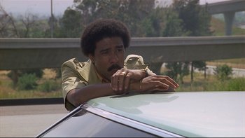 Movie still from “California Suite” (1978), directed by Herbert Ross – A man leaning on the hood of a car on the side of the road; Close Up shot, Low angle