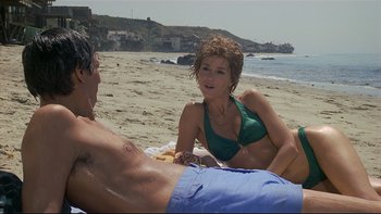 Movie still from “California Suite” (1978), directed by Herbert Ross – A man and a woman sitting on a towel on the beach; Medium shot, High angle