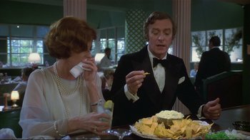 Movie still from “California Suite” (1978), directed by Herbert Ross – A man and a woman sitting in front of a table with food on top of it; Medium shot, Over the shoulder angle