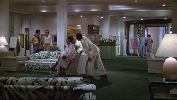 Movie still from “California Suite” (1978), directed by Herbert Ross – Two women sitting on a couch in a room with a man standing next to the couch; Wide shot, High angle