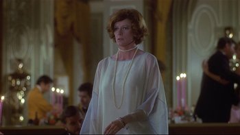 Movie still from “California Suite” (1978), directed by Herbert Ross – A woman in a white dress and pearls standing in front of candles; Medium shot, Over the shoulder angle