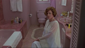 Movie still from “California Suite” (1978), directed by Herbert Ross – A woman sitting in a bathroom wearing a white dress; Wide shot, High angle
