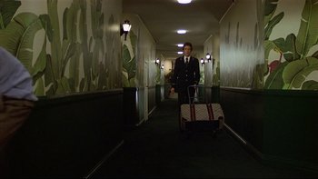 Movie still from “California Suite” (1978), directed by Herbert Ross – A man in a suit and tie pulling a suitcase; Wide shot, Low angle