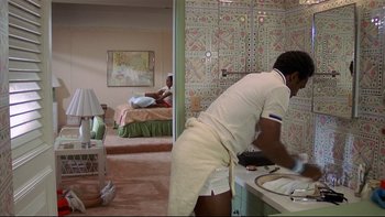 Movie still from “California Suite” (1978), directed by Herbert Ross – A man in white shirt and white shorts washing dishes in a bathroom; Wide shot, Low angle
