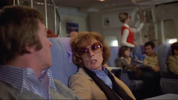 Movie still from “California Suite” (1978), directed by Herbert Ross – A woman sitting on a seat on an airplane; Medium shot, Over the shoulder angle