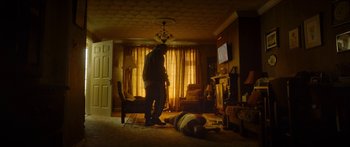 Movie still from “Calm with Horses” (2019), directed by Nick Rowland – A man standing in a living room next to a man lying on the ground; Wide shot, Low angle