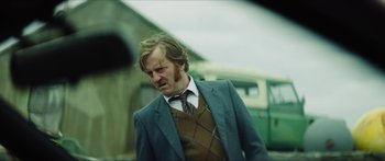 Movie still from “Calm with Horses” (2019), directed by Nick Rowland – A man in a suit and tie standing next to a car; Medium shot, Over the shoulder angle