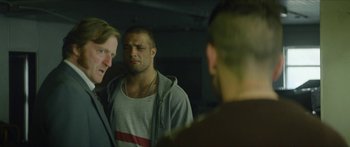 Movie still from “Calm with Horses” (2019), directed by Nick Rowland – A man looking at himself in the mirror while two other men look on; Medium shot, Over the shoulder angle