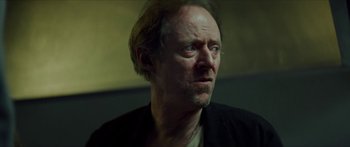 Movie still from “Calm with Horses” (2019), directed by Nick Rowland – A man with a beard and a necklace looking at the camera; Close Up shot, Low angle