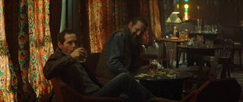 Movie still from “Calm with Horses” (2019), directed by Nick Rowland – Two men sitting at a table with drinks and food; Medium shot, Over the shoulder angle
