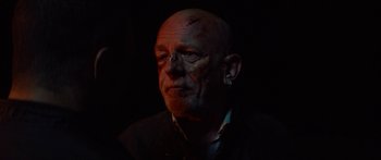Movie still from “Calm with Horses” (2019), directed by Nick Rowland – An old man with a shaved head and a piercing; Close Up shot, Over the shoulder angle