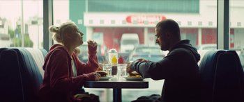 Movie still from “Calm with Horses” (2019), directed by Nick Rowland – A man and a woman sitting at a table eating a sandwich; Medium shot, Over the shoulder angle