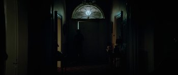 Movie still from “Calm with Horses” (2019), directed by Nick Rowland – A person standing in a dark room in front of a window; Wide shot, Over the shoulder angle